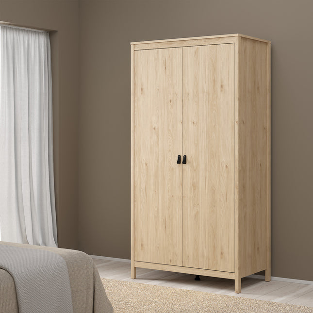 Two-door wardrobe with a light wood finish and black handles, standing on four legs against a neutral wall