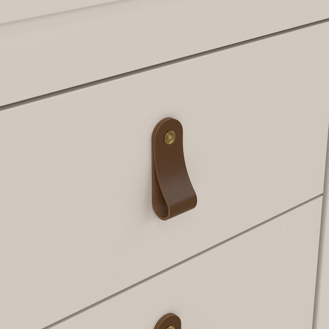 Close-up of a drawer handle made of brown leather with a brass stud, attached to a smooth, pale surface