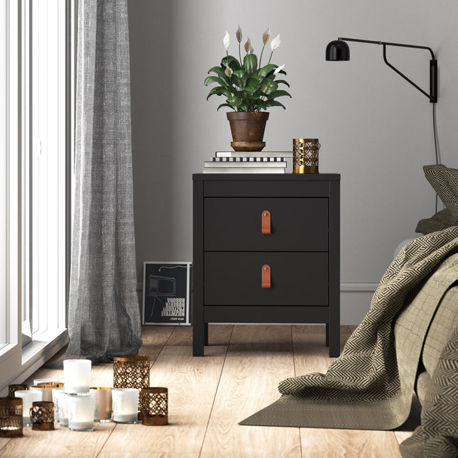 Bedside table with two drawers, black finish, leather strap handles, placed beside a bed with decorative cushions