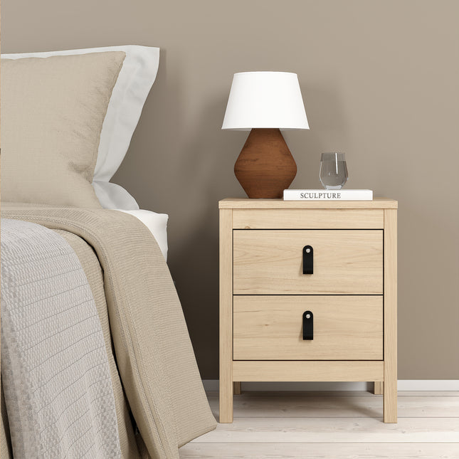 Square bedside table with two drawers, natural wood finish, black handles, beside a lamp and a glass of water