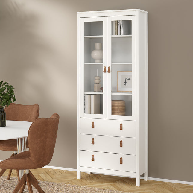 Tall cabinet with glass doors, three drawers, and wooden handles, finished in white. Shelves display decorative items