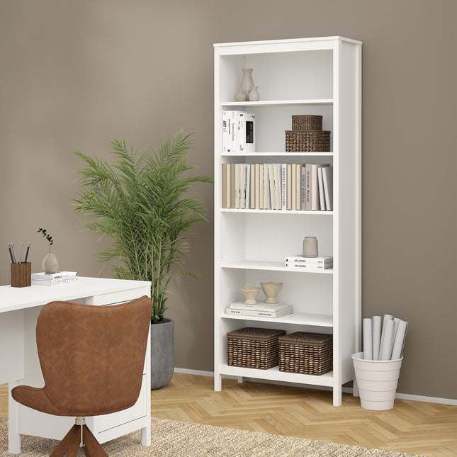 Tall white bookcase with five open shelves, featuring decorative items and woven baskets, beside a brown chair and plant