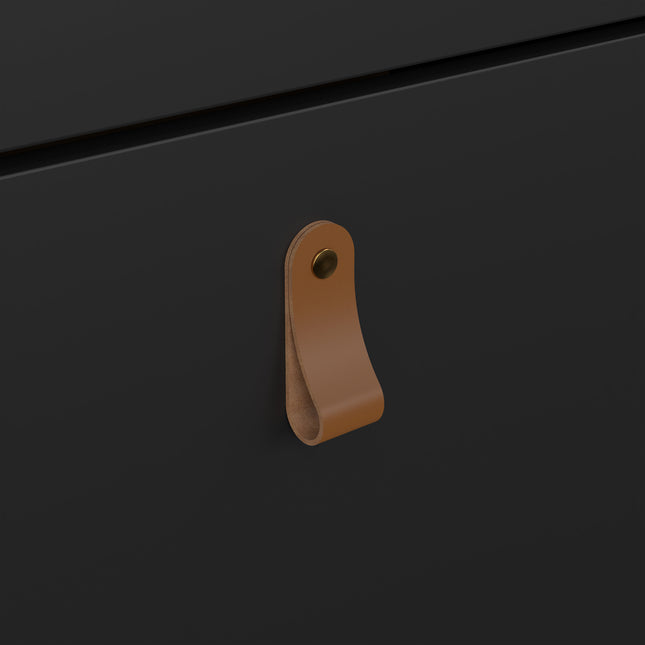 Leather handle in tan with a brass stud, attached to a sleek black cabinet door