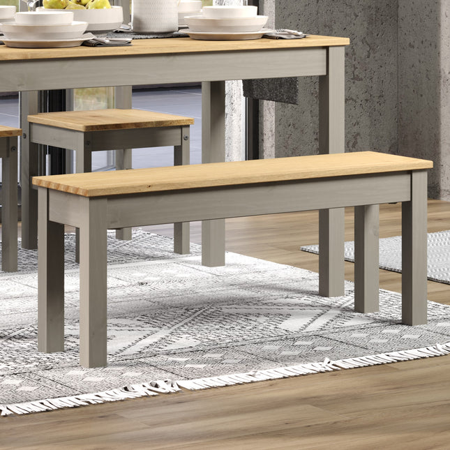 Bench with a rectangular wooden top in light wood and grey legs, placed on a patterned rug beside a dining table