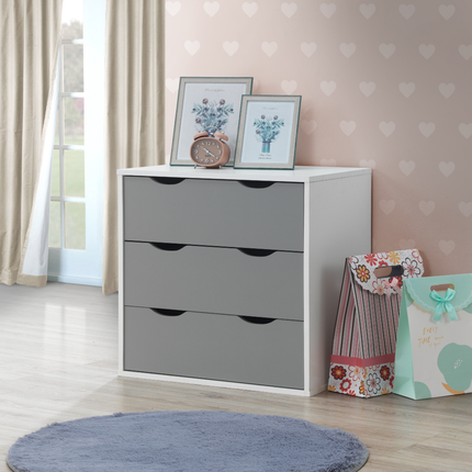 Three-drawer chest with a white frame and grey drawers, featuring cut-out handles, placed against a pastel wall