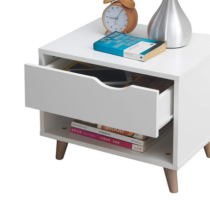 Bedside table with one drawer and open shelf, finished in white with wooden legs, displaying books and a clock