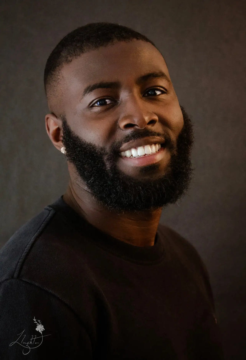 A smiling man with a full black beard and short-cropped hair, wearing a dark gray crew-neck t-shirt.
