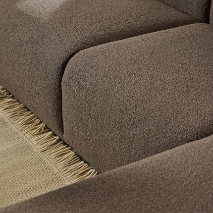 Close-up of brown boucle upholstery and rounded seat seams on chaise with fringed rug edge