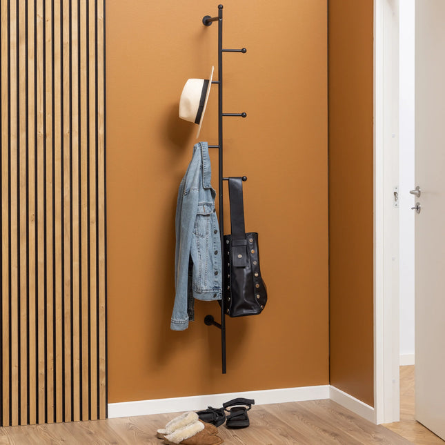 Close-up of black steel wall-mounted coat rack with staggered ball-tipped hooks and jacket and bag hanging